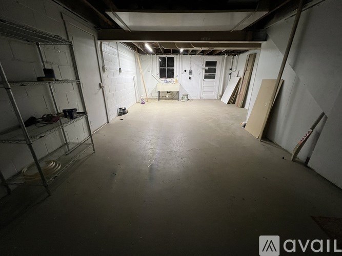 A large, empty room with a concrete floor and walls, some shelving units, and a window with blinds.