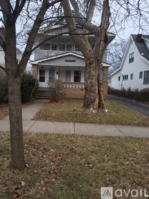 A house with a white front porch and a tree in front of it.