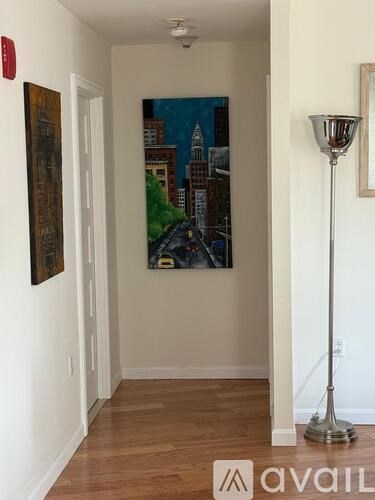 A hallway with a painting of a cityscape on the wall and a floor lamp on the right.