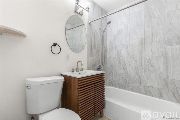 A bathroom with a white toilet, a round mirror, a sink, and a bathtub.