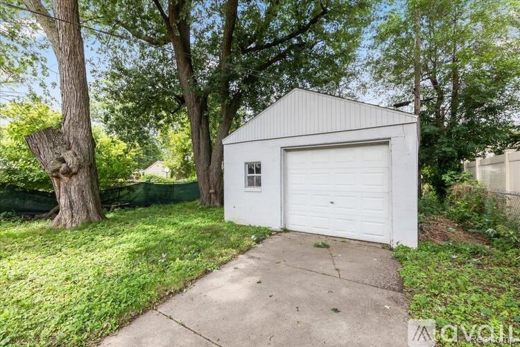 A small white garage is situated on a concrete slab in a grassy area.