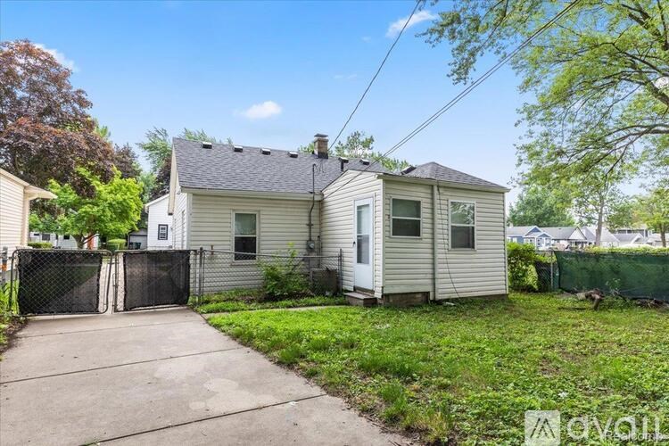 A house with a grey roof and a white door is surrounded by a green lawn and trees.