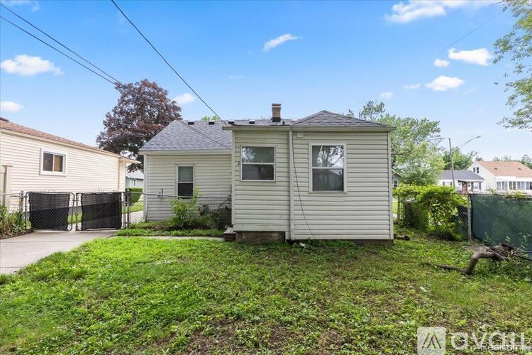 A small house with a grey roof and a white exterior is surrounded by a grassy area.