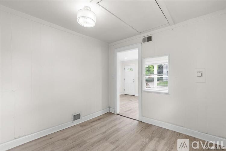 A room with white walls and wooden flooring, with a doorway leading to another room.