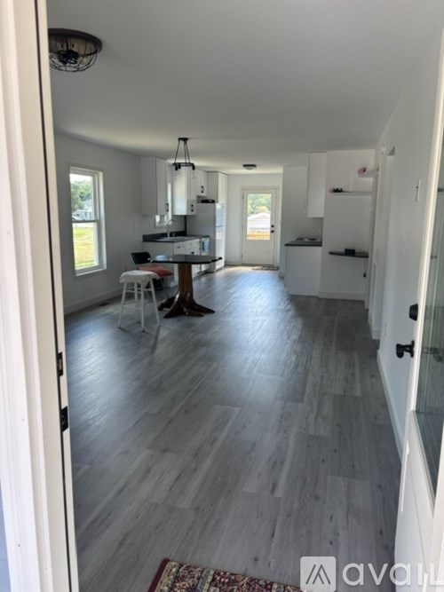 A hallway with a rug on the floor and a kitchen in the background.