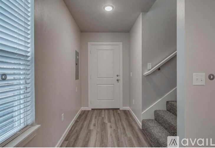 A hallway with a white door and stairs on the right side.