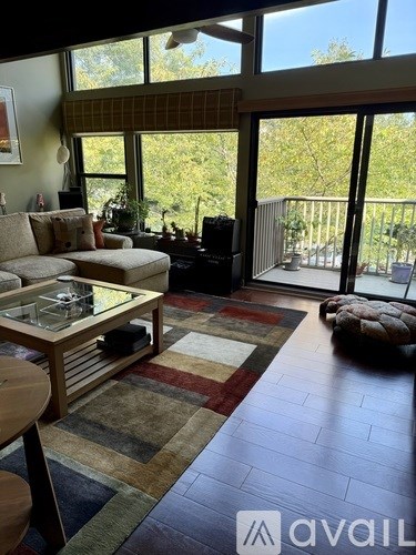 A living room with a couch, coffee table, rug and a balcony.