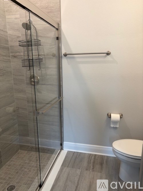 A bathroom with a toilet, a glass shower stall, and a towel bar.