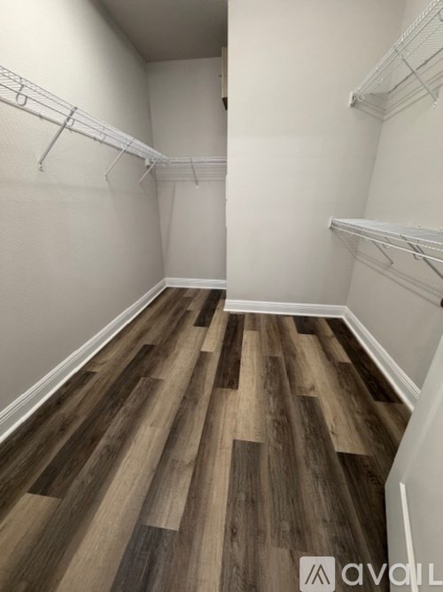 A room with white walls and wood flooring with a white shelf on the wall.