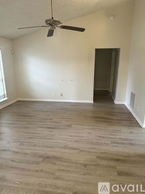 A room with a fan and wooden flooring.