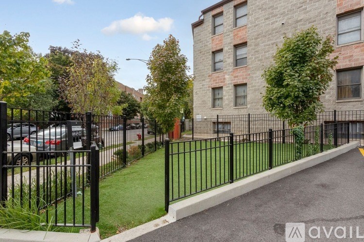 A black iron fence surrounds a green lawn in front of a brick building.