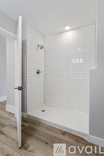 A white tiled shower with a door open to a hallway.