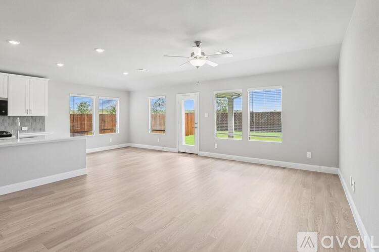 A spacious living room with a kitchen area and a ceiling fan.