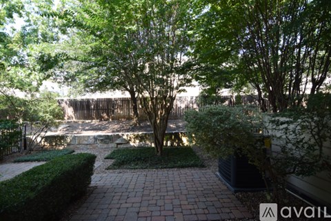 A backyard with a brick walkway and a tree in the center.