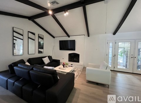 A black leather couch sits in a spacious living room with a fireplace and a flat screen TV mounted on the wall.