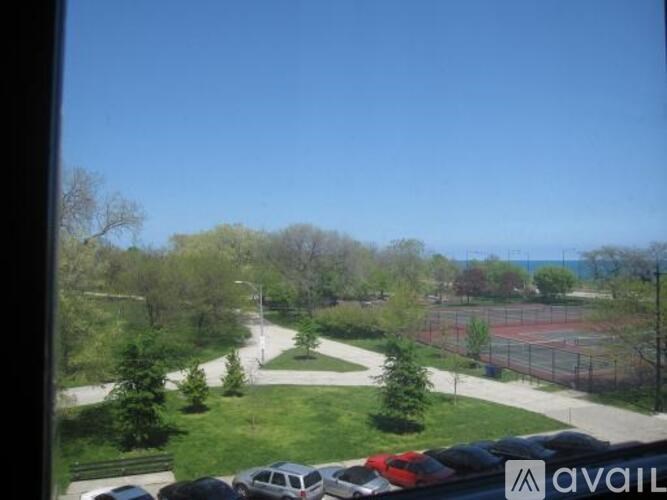 A view from a window looking out at a tennis court and a parking lot.