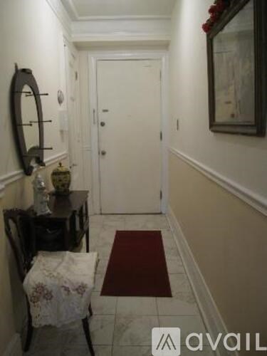 A hallway with a mirror, a table with a vase and a chair.