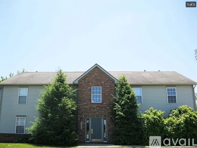 A house with a grey siding and a brick chimney is surrounded by trees.