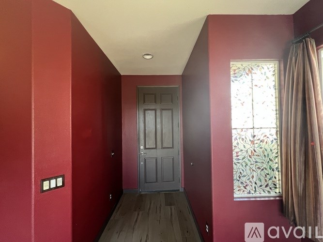 A hallway with a wooden floor, a grey door, and a stained glass window.