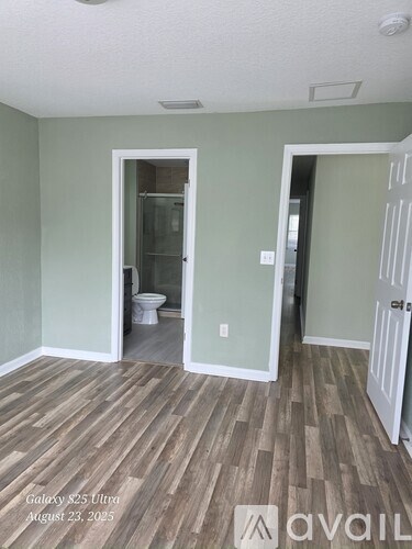 A room with wood flooring and two doors, one of which is open to a bathroom.