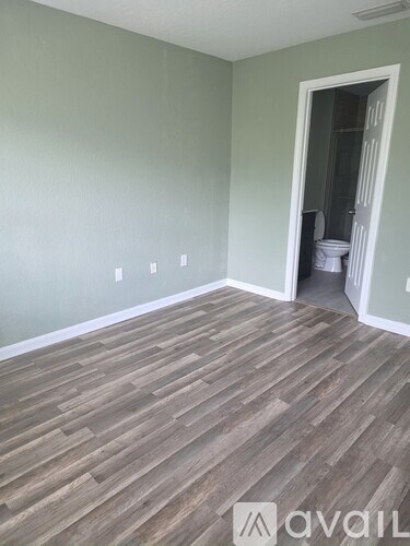 A room with wooden flooring and a doorway leading to a bathroom.