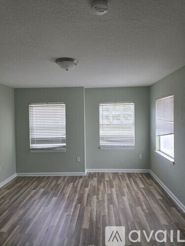A room with wooden floors and two windows with blinds.