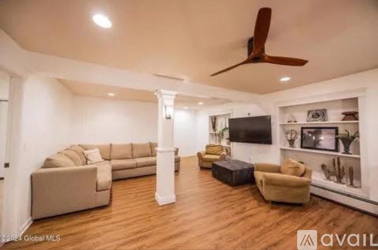 A spacious living room with a beige sofa set, a television, and a wooden floor.