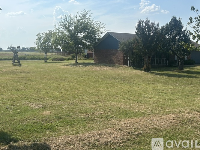 A grassy field with a house and trees in the background.