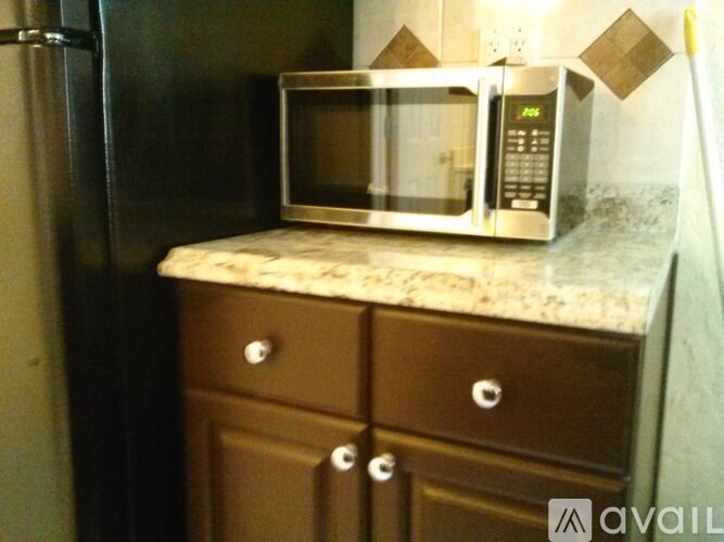 A silver microwave oven is on a countertop above a brown cabinet with two drawers.