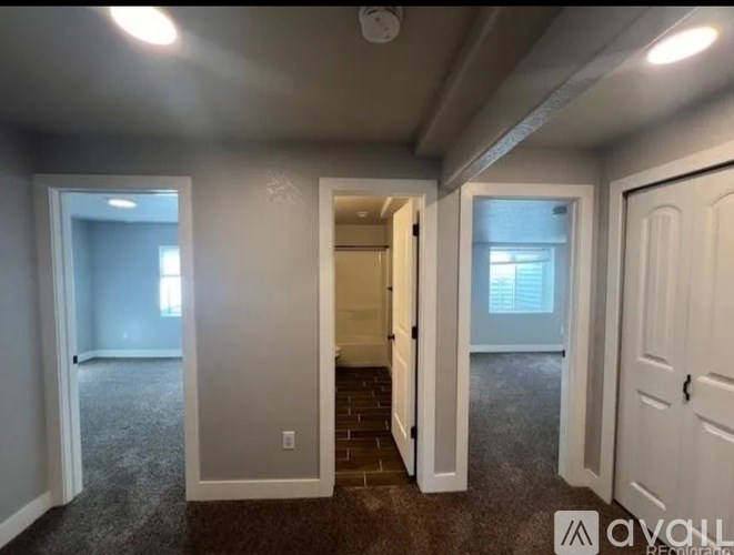 A room with carpeted floors and white walls, with a door on the right and a window on the left.