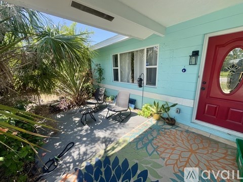 A blue house with a red door and a patio with a table and chairs.
