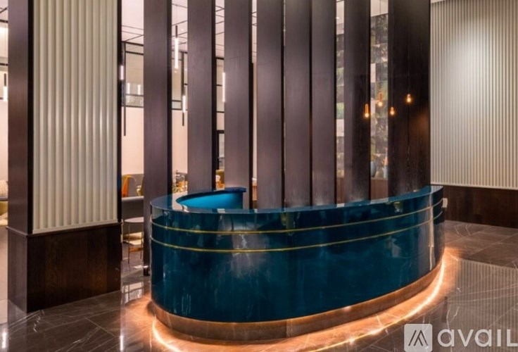 A blue circular table is in the middle of a room with a dark floor and a wall with columns.