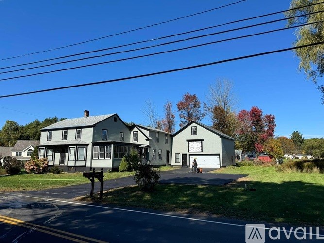 A house with a grey roof and white walls is surrounded by trees with autumn leaves.