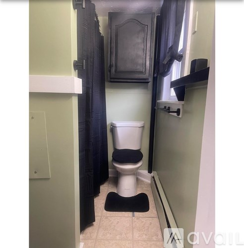 A white toilet with a black seat and a black mat in a bathroom.