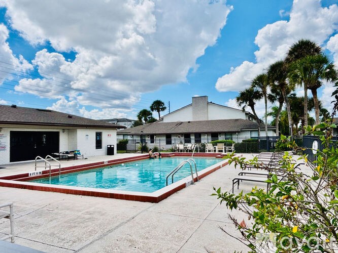 A pool surrounded by a concrete patio and a building in the background.