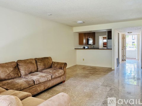 A living room with a brown couch and a kitchen in the background.