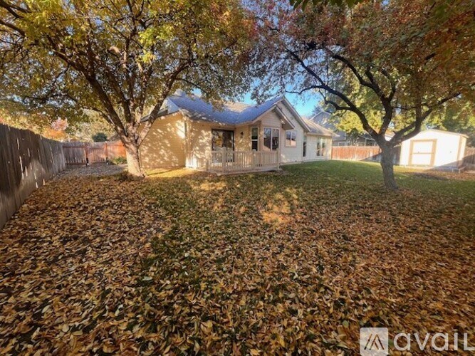 A house with a fence and trees with fallen leaves in front.
