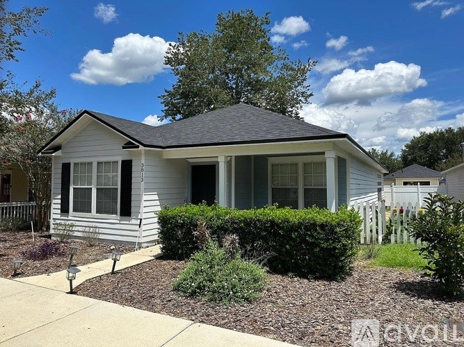 A small house with a grey roof and white walls is surrounded by a garden.