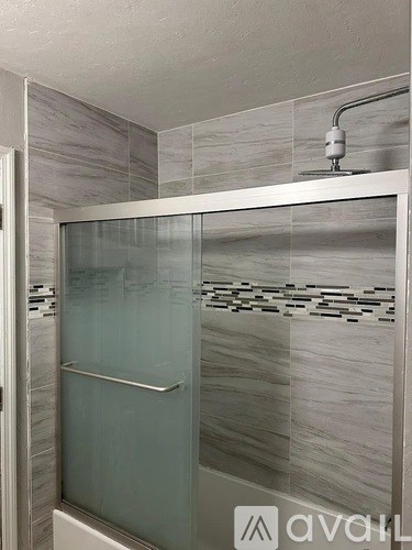 A shower area with a glass door and a wall of tiles.