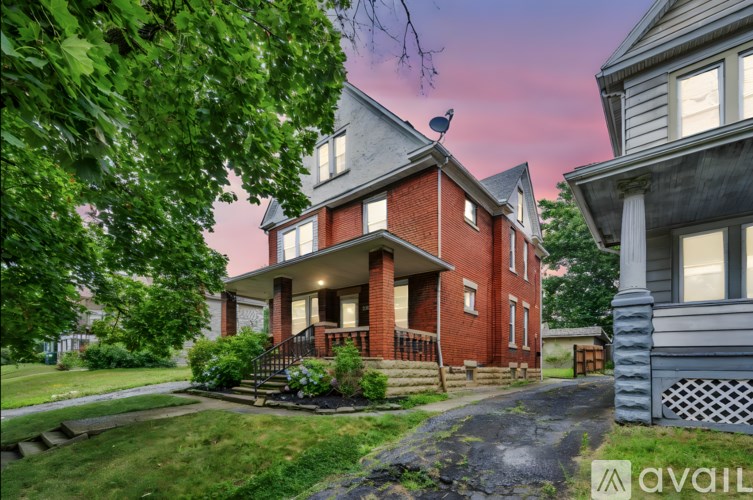 A house with a red brick exterior and a grey roof is surrounded by greenery.