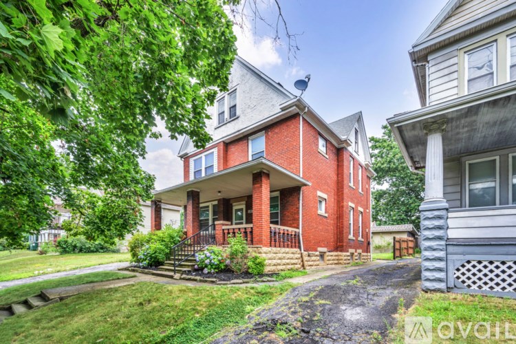 A red brick house with a porch and a tree in front.