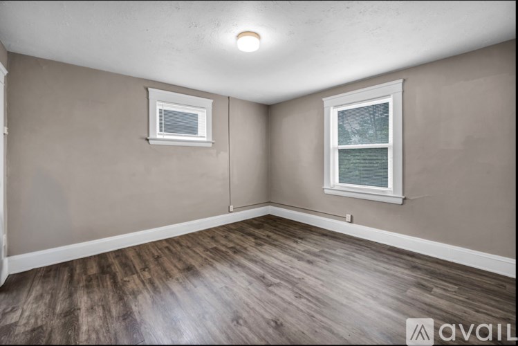 A room with wooden flooring and two windows.