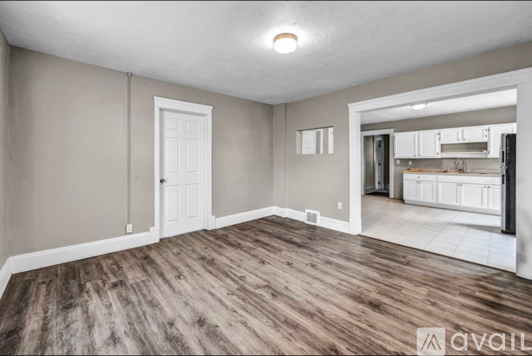 A room with wooden flooring and white walls, with a door leading to another room.