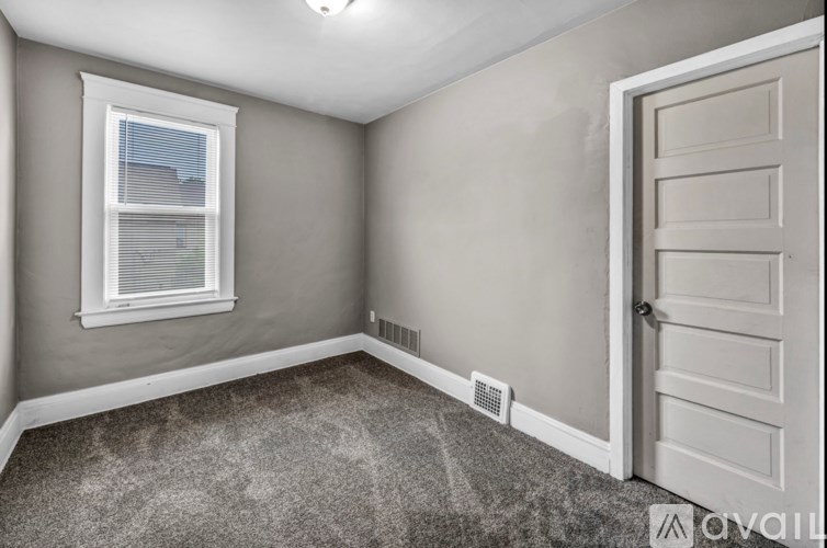 A room with a carpeted floor, a window with blinds, a door, and a wall-mounted air vent.