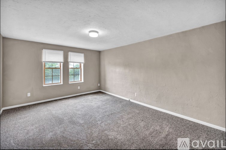 A room with grey carpet and two windows.