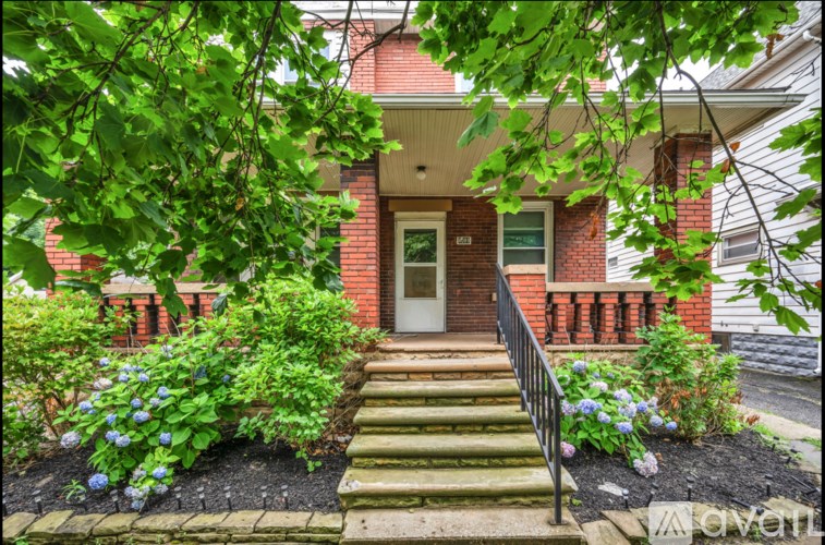 A house with a red brick facade and a white door is surrounded by greenery.