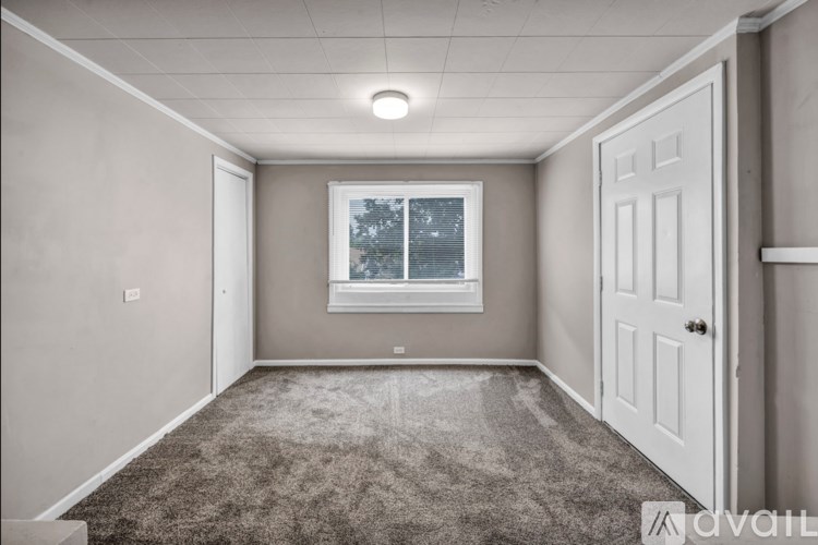 A room with a carpeted floor, a window with blinds, and a white door.