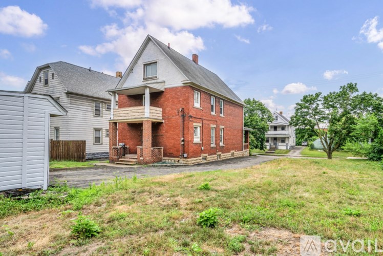 A house with a red brick exterior is surrounded by a grassy area and other houses.