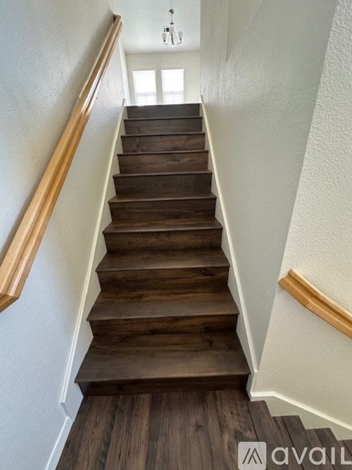 A wooden staircase with a white wall on one side and a window on the other.