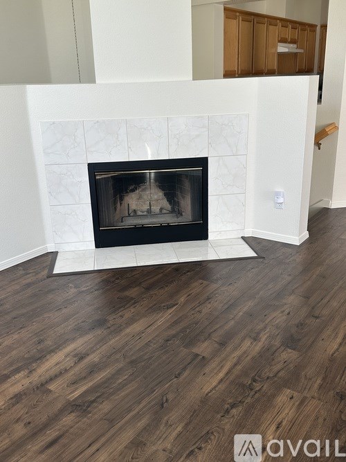 A white fireplace with a black grate in a room with wooden floors.